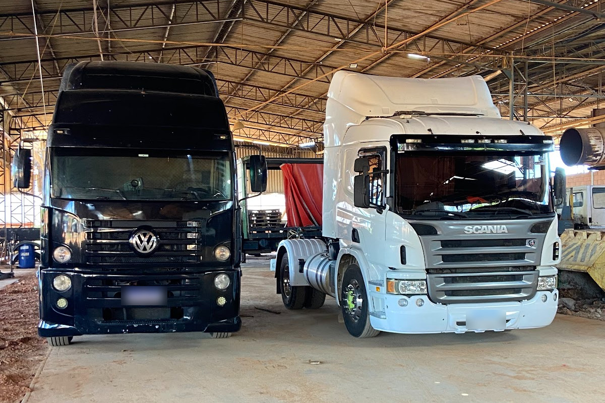 Dois cavalos mecânicos, um Volkswagen preto e um Scania branco, lado a lado em um galpão