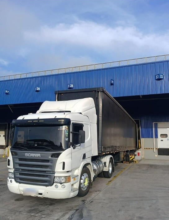 Carreta Scania branca encostada na doca de um galpão azul em Feira de Santana