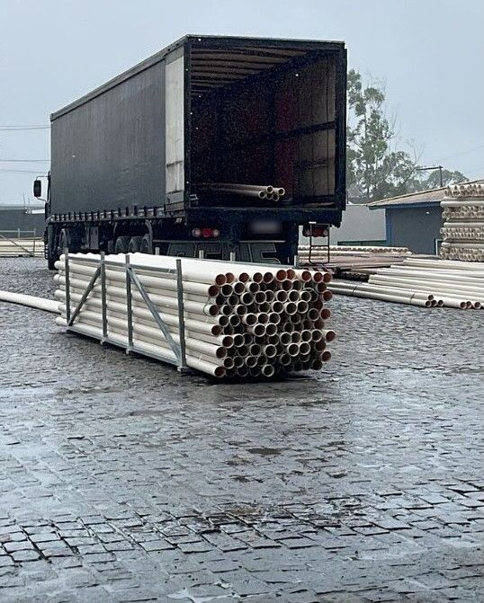 Descarga de tubos brancos ao lado da carreta em Feira de Santana, em dia de chuva